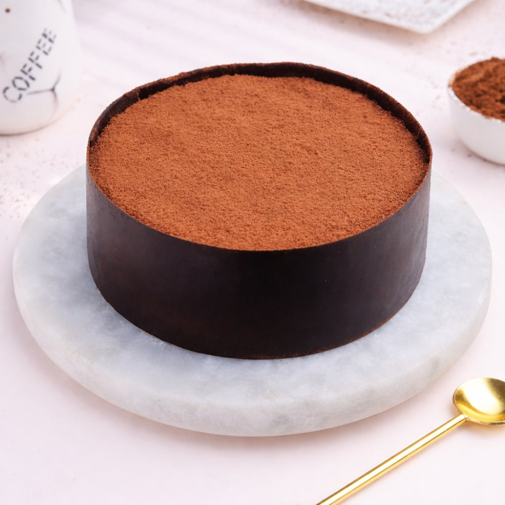 Round Choco Dream Cake with rich cocoa dusting and a dark chocolate band, on a white marble plate.