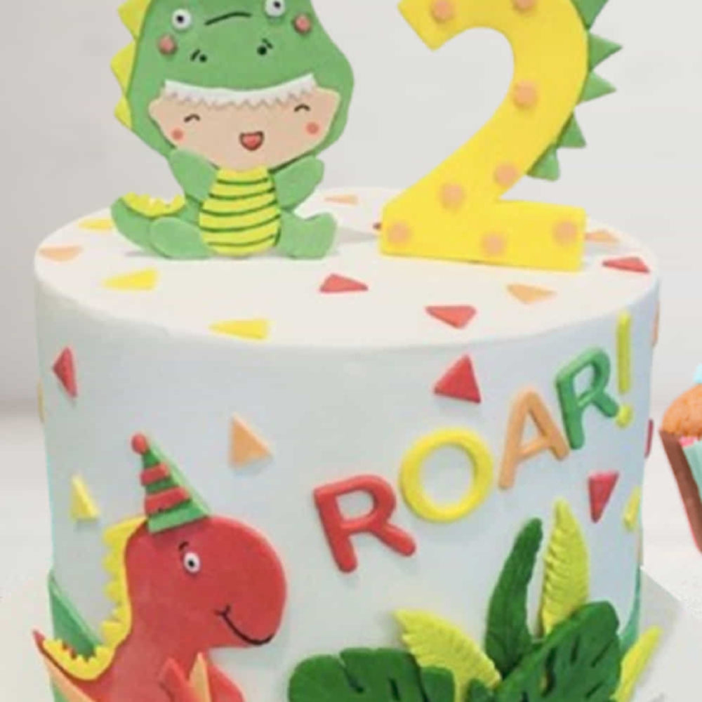Children's birthday cake with dinosaur decorations and the number 2 candle.