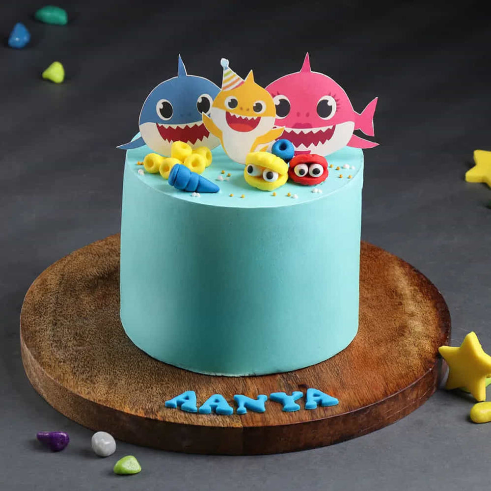 light blue Baby Shark birthday cake featuring paper character toppers and colorful edible sea shells.