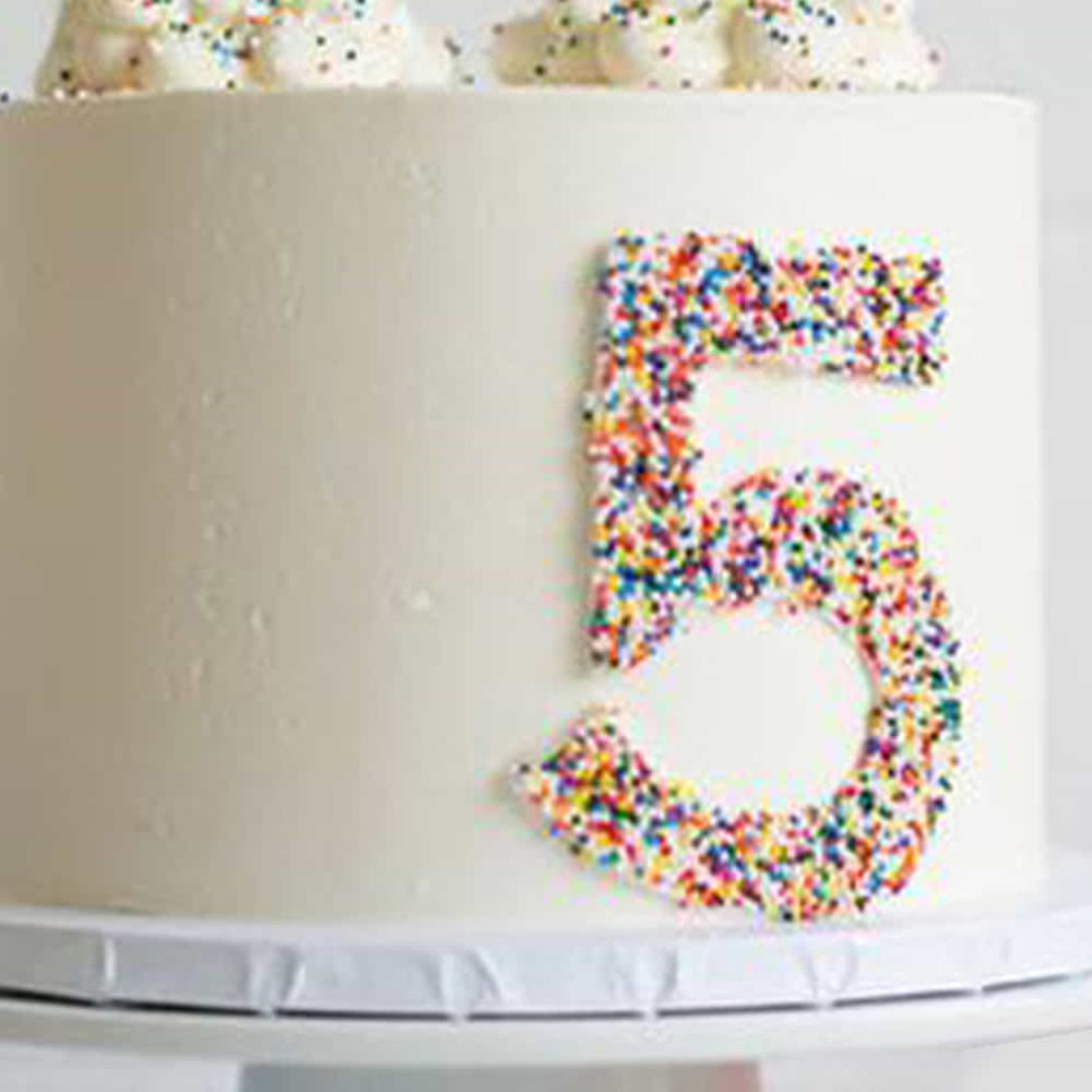 White cake with a number 5 made of colorful sprinkles
