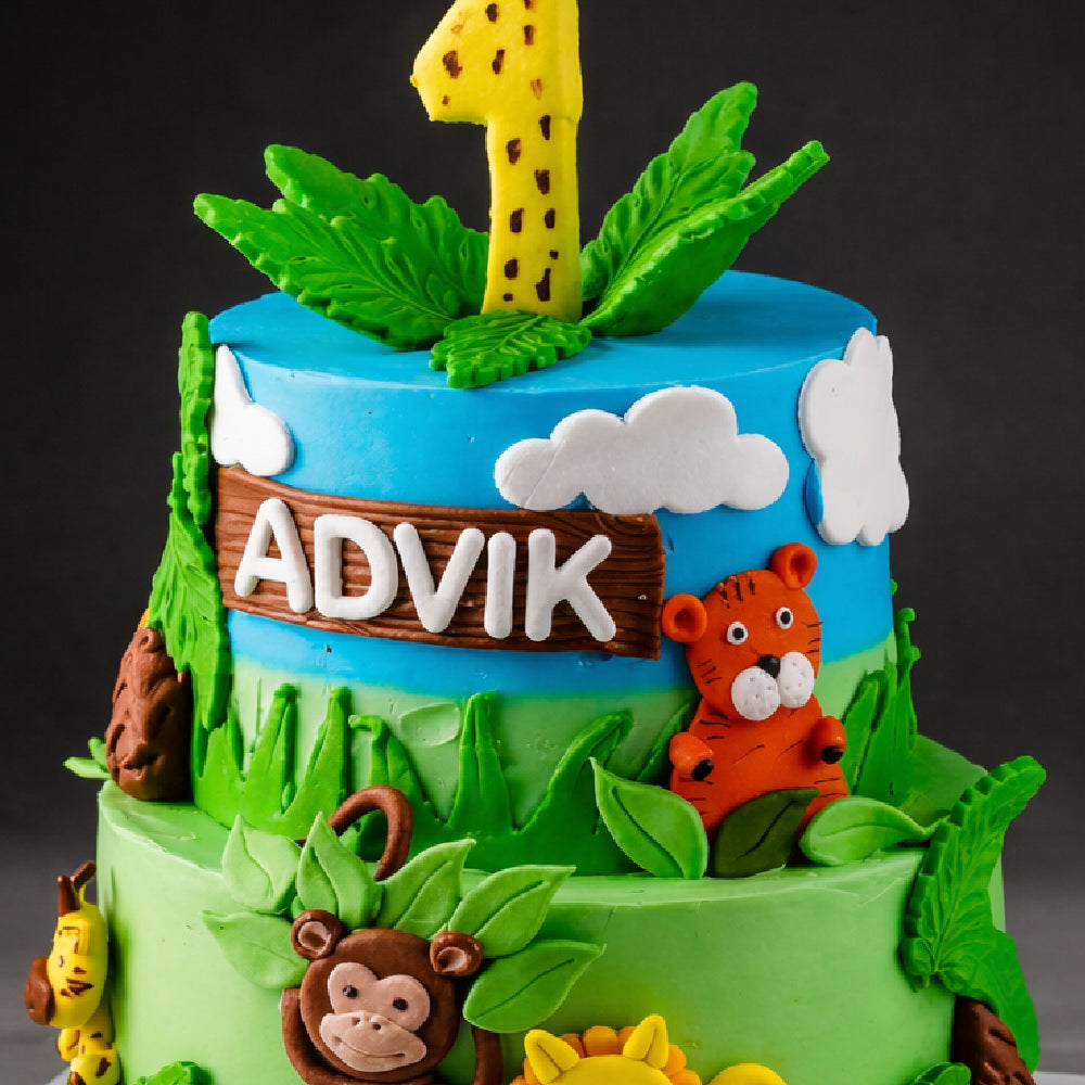 Two-tier jungle theme designer cake with name Advik, number one topper, and fondant animals like tiger and monkey, decorated with leaves and clouds for a first birthday celebration.