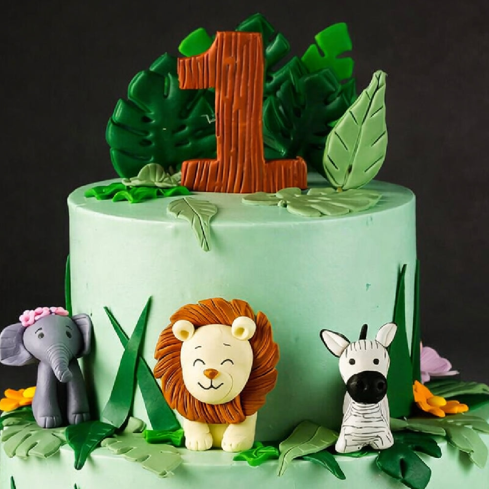 Jungle-themed designer cake with number one topper, featuring fondant animals like lion, elephant, and zebra with green leaves, perfect for a first birthday celebration.