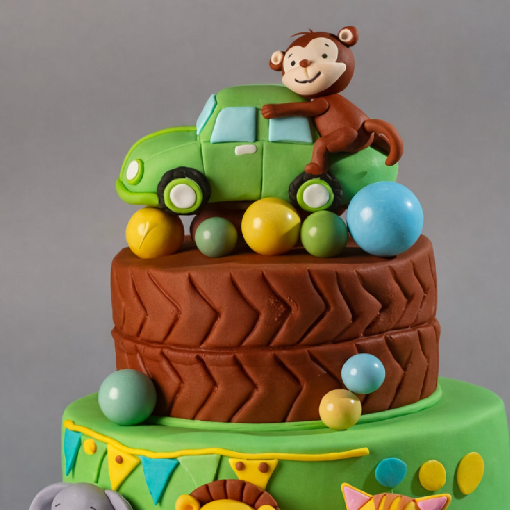Cute kids designer cake with a monkey sitting on a green car topper, colorful balls, and jungle theme decoration, perfect for a birthday celebration.
