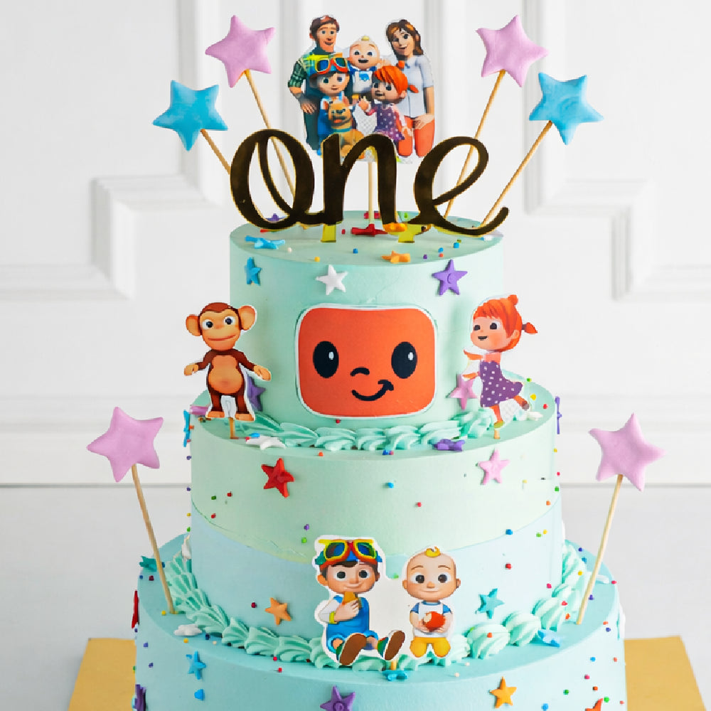 Three-tier kids designer cake with cartoon characters, number one topper, star decorations, and colorful theme, perfect for a first birthday celebration.