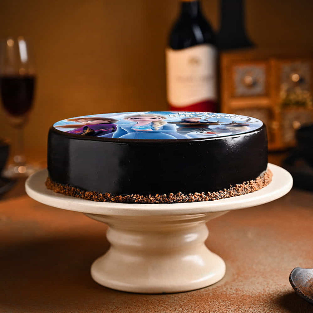 Chocolate cake with a printed design on a white stand, with wine bottles and glasses in the background.
