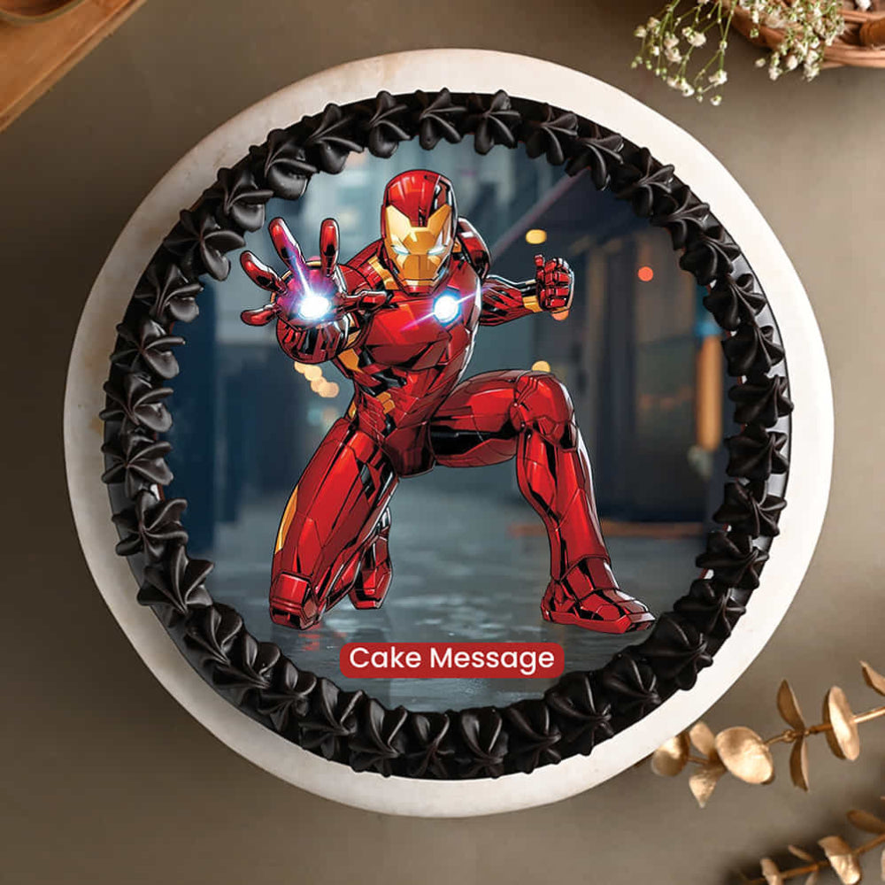 A round cake with a black piped frosting border, featuring an edible image of a red armored superhero in a dynamic pose with a glowing hand at the center. The cake sits on a neutral surface with decorative elements around it, and a placeholder text reading “Cake Message” appears on the image.