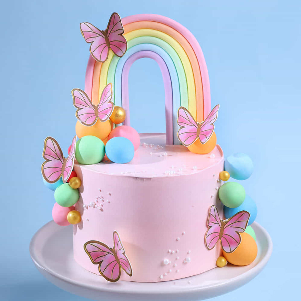 Pink cake with rainbow, butterflies, and colorful balls on a blue background