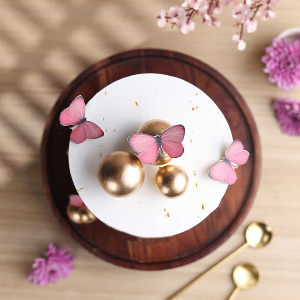 Gold earrings with pink butterfly designs on a white dish, surrounded by pink flowers.