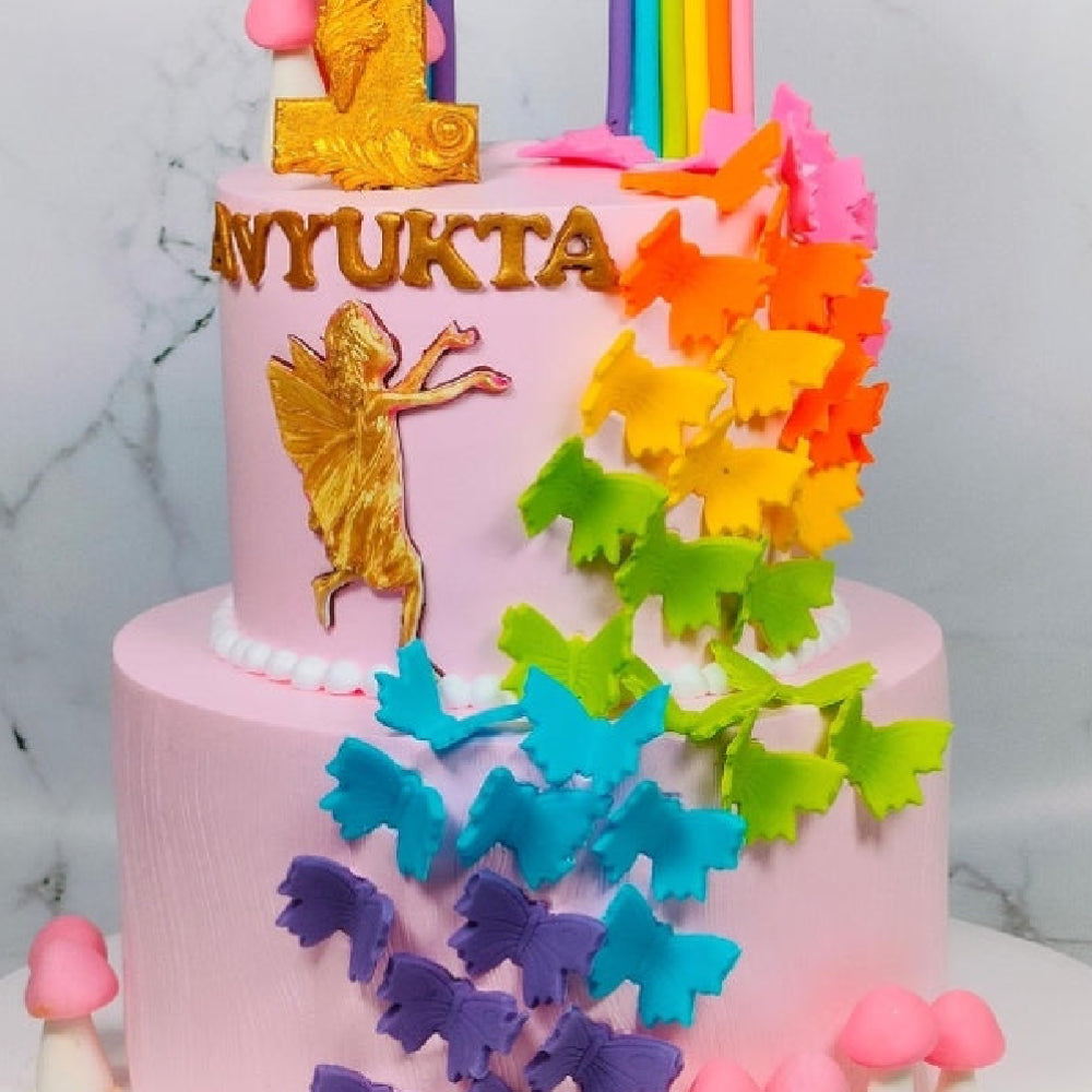 Colorful birthday cake with butterfly decorations and a fairy figure on a marble background