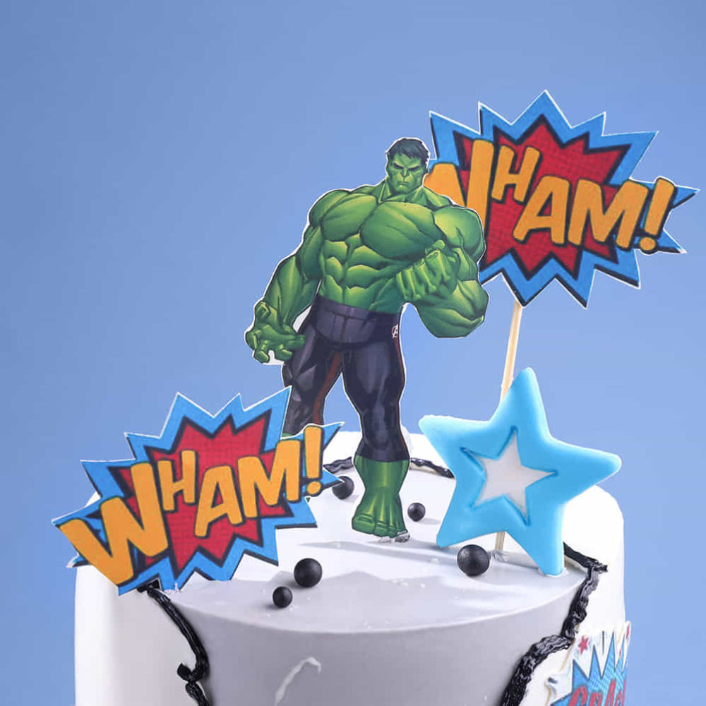 Cake topper with Hulk figure and 'WHAM!' text on a blue background