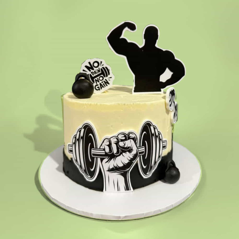 Cream and black round cake with a fitness theme, featuring a barbell illustration on the side, a flexing silhouette topper, and a “No Pain No Gain” sign on top, set against a light green background.