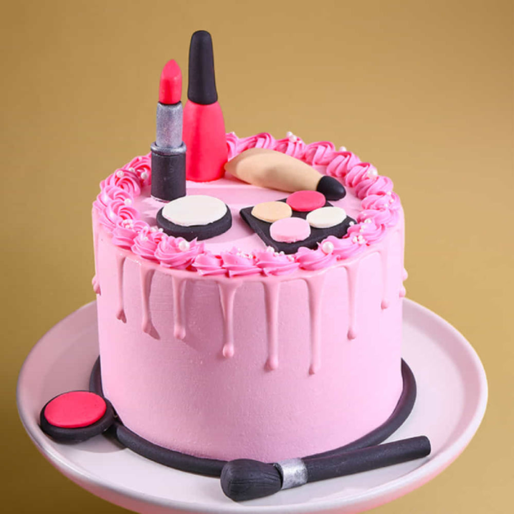 Pink drip designer cake decorated with makeup items like lipstick, nail polish, foundation, and brushes on top, placed on a cake stand with a soft background.