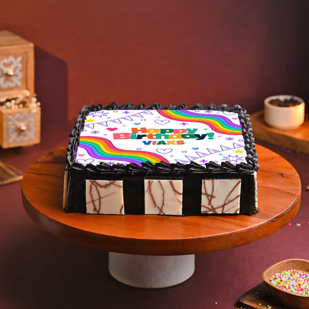 Birthday cake with colorful icing on a wooden cake stand against a dark background