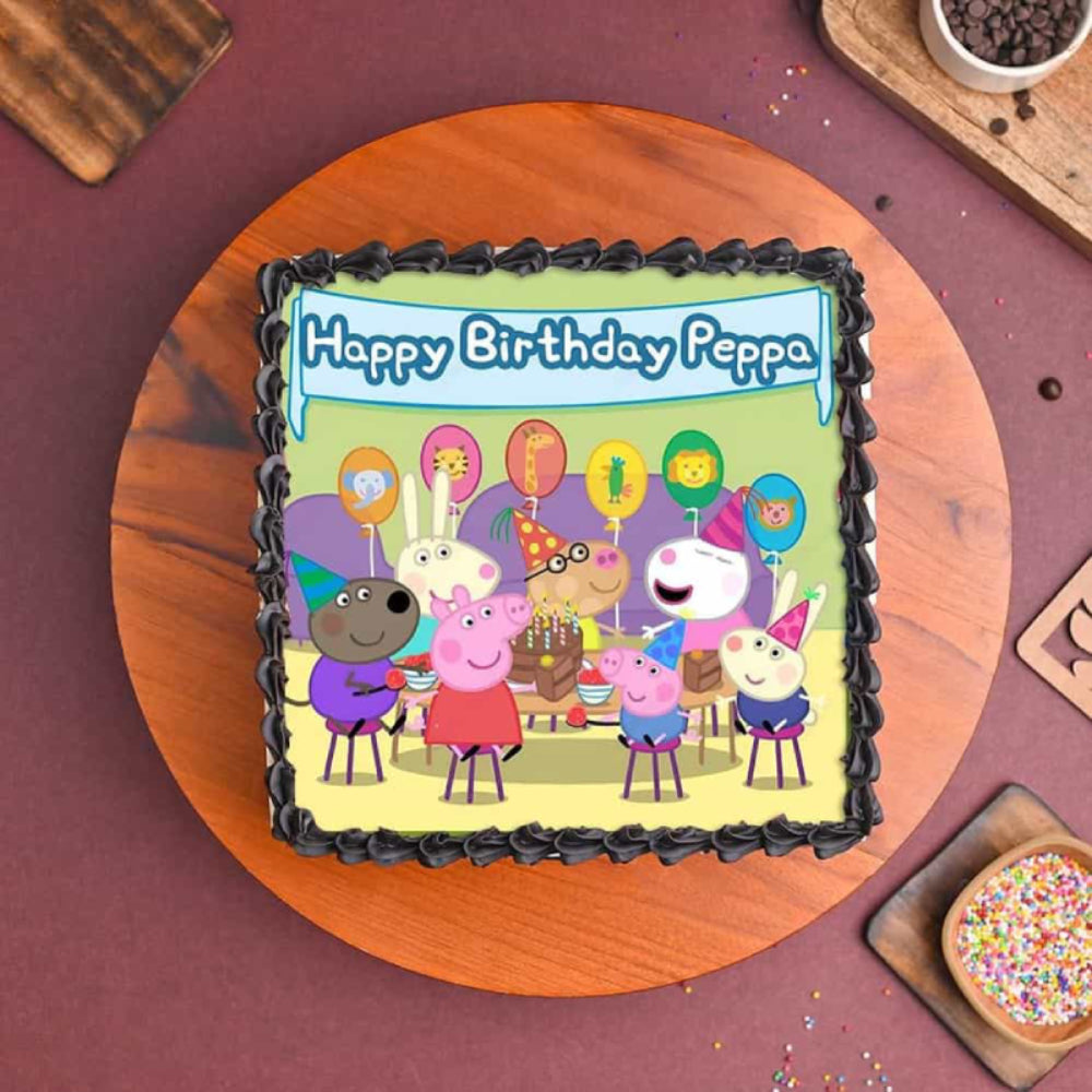 A square chocolate birthday cake featuring a colorful Peppa Pig party scene edible topper. The cake is finished with dark chocolate piping and white chocolate square accents on the sides, displayed on a wooden cake stand.