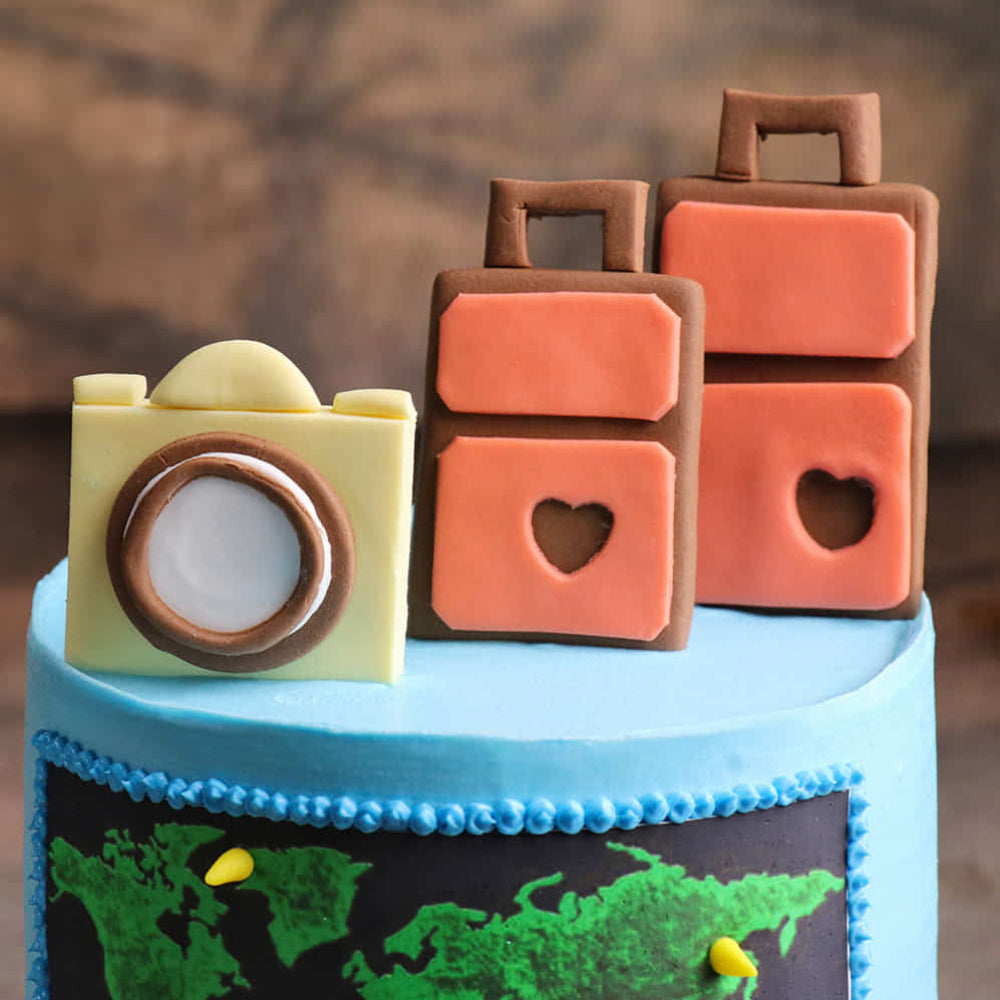 Blue travel cake with world map, camera, and suitcase toppers.