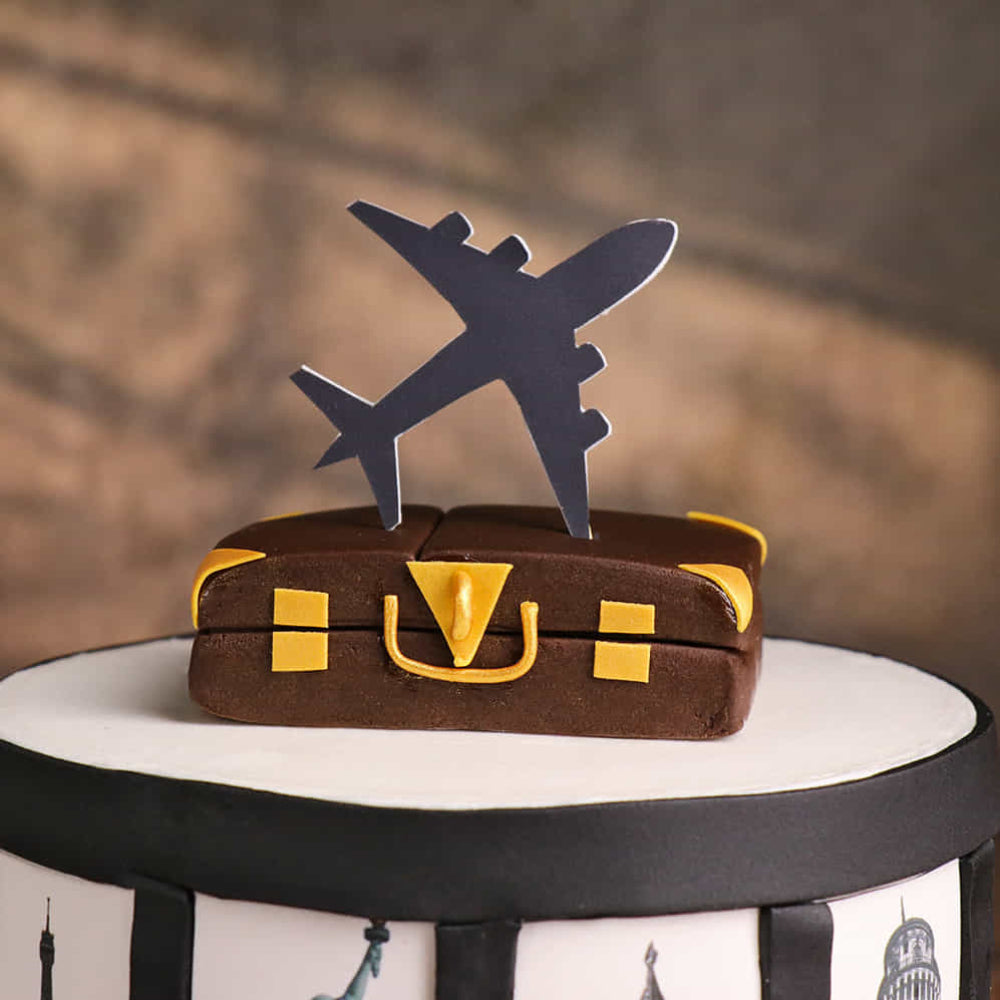 Travel-themed cake with world landmarks, suitcase topper, and airplane silhouette.