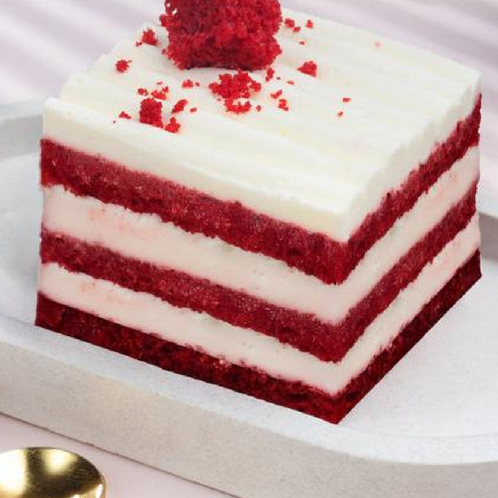 Square red velvet pastry with alternating layers of red cake and white cream cheese frosting, topped with red crumbs.