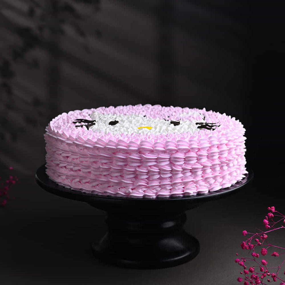 Pink frosted cake with a simple cartoon face design on top, displayed on a black stand.