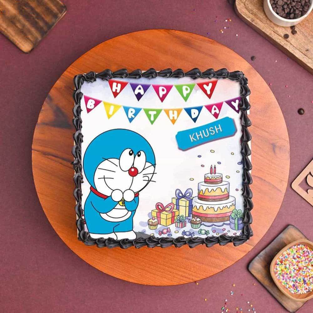 Birthday cake with Doraemon design and personalized name on a wooden board.