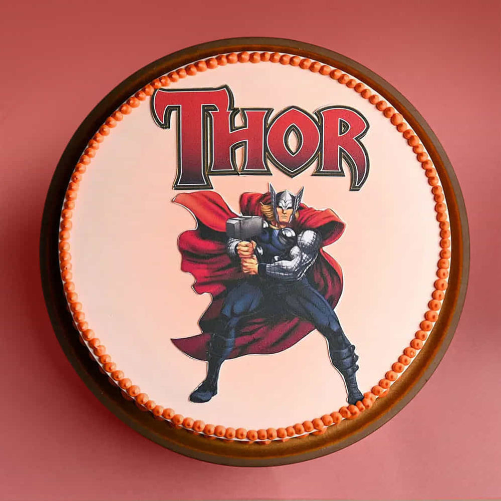 Thor cake with red cape and hammer on a pink background