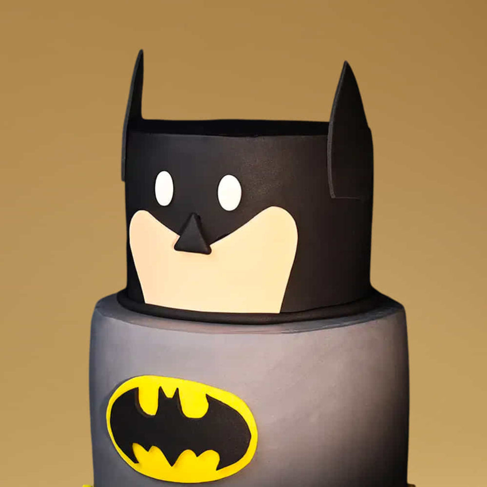 Cake designed to resemble a Batman character with a yellow bat symbol on a brown background