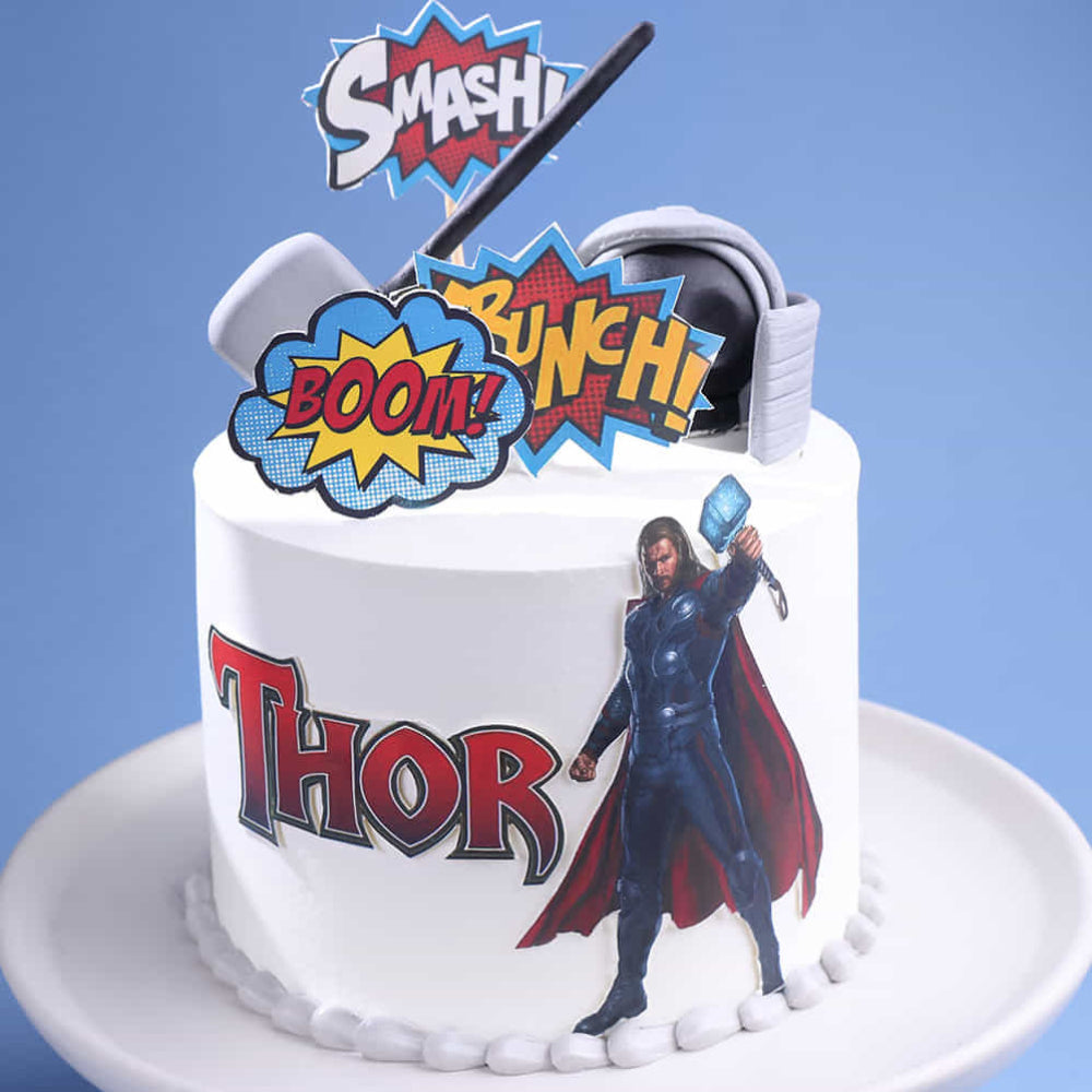 Thor-themed cake with superhero figurine and colorful text on a blue background