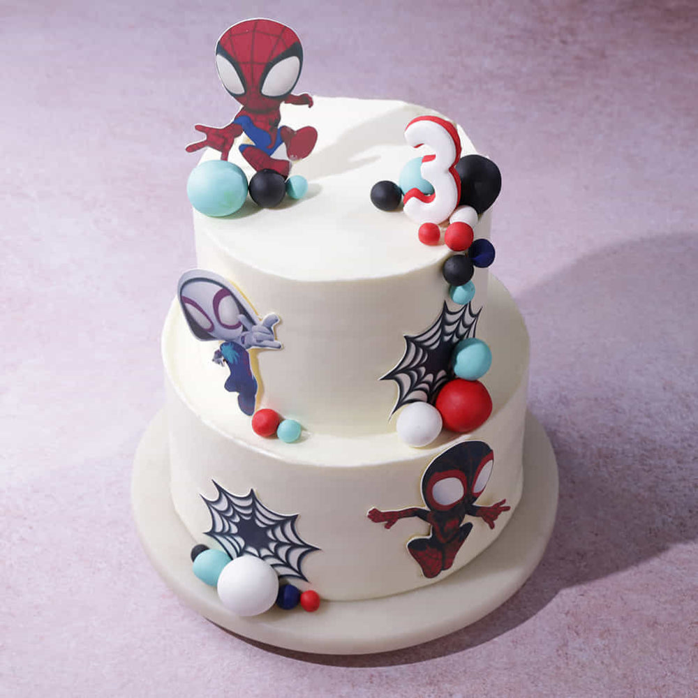 Two-tier cake decorated with Spider-Man figures and colorful elements on a light purple background