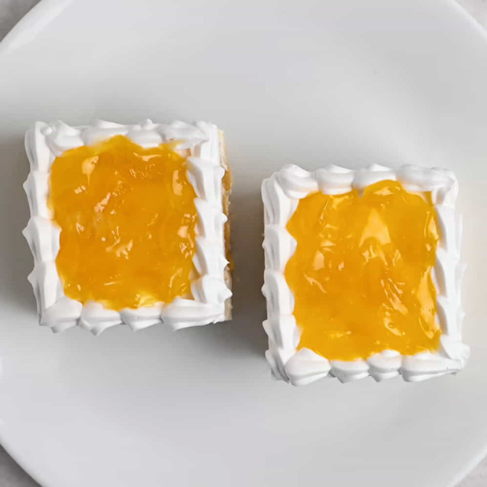 Two square pineapple pastries with white whipped cream borders and a bright yellow fruit filling on a white plate.
