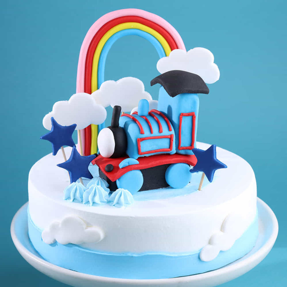 Blue train and rainbow themed birthday cake with 3D locomotive topper and fondant cloud decorations.