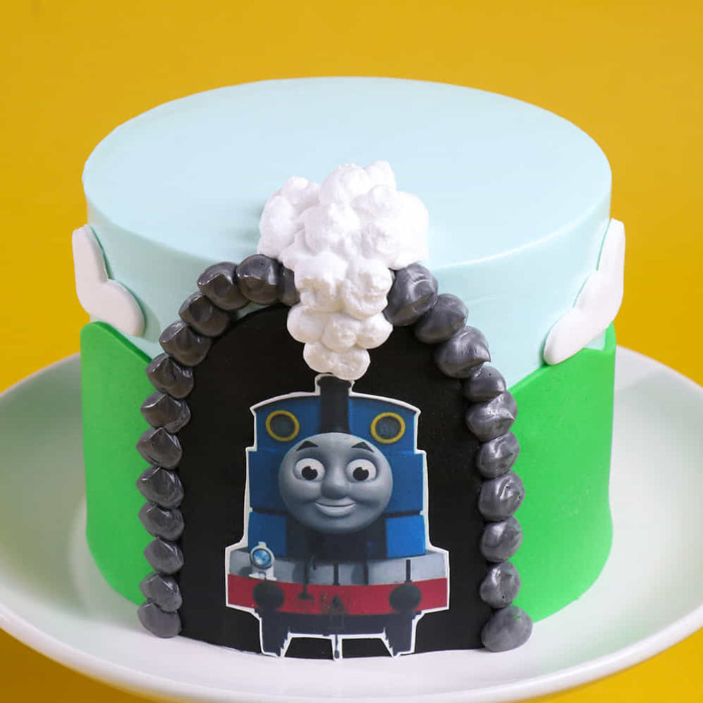 Custom Thomas & Friends birthday cake with edible train engine image, green hills, and cloud fondant decorations.