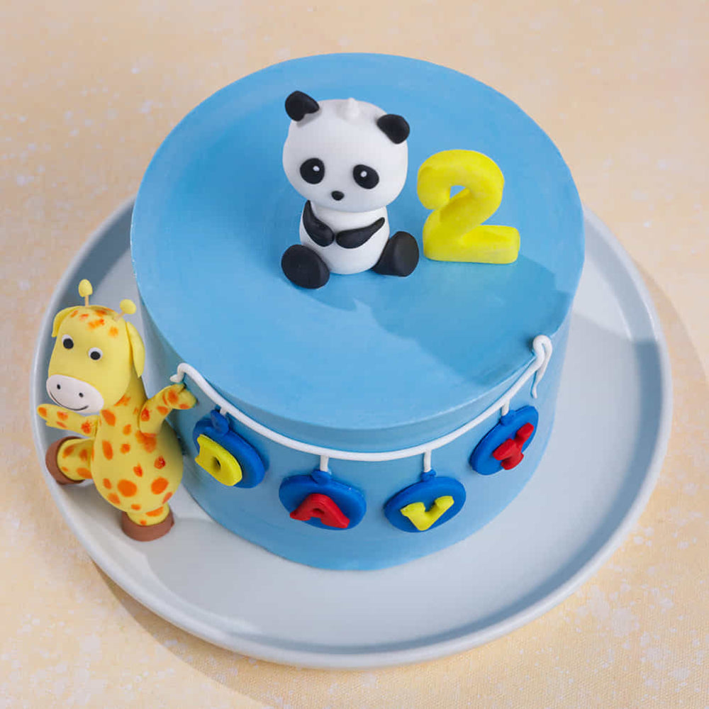 A light blue fondant cake for a second birthday, featuring a 3D fondant panda topper, a yellow giraffe standing on the side, and a "DAVY" name banner with a yellow number 2. Top view