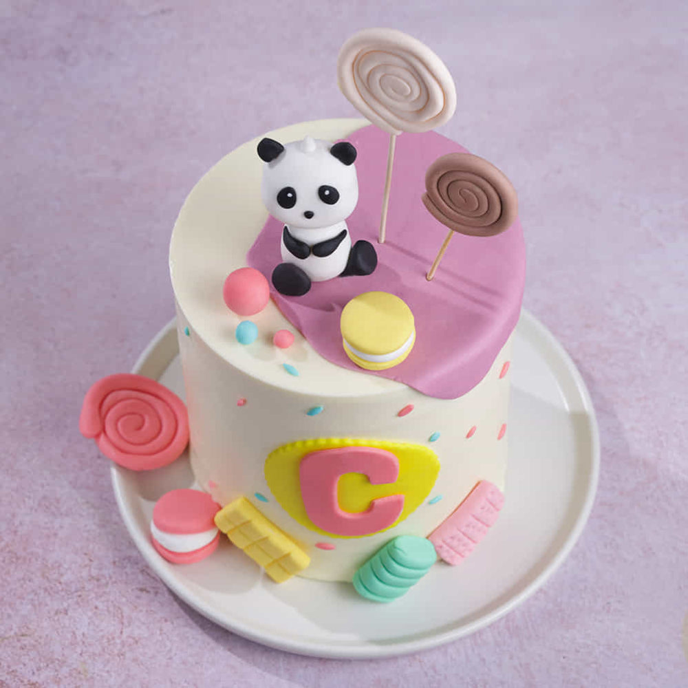 A tall, birthday cake with white frosting, decorated with colorful fondant sweets and topped with a cute panda figure. top view