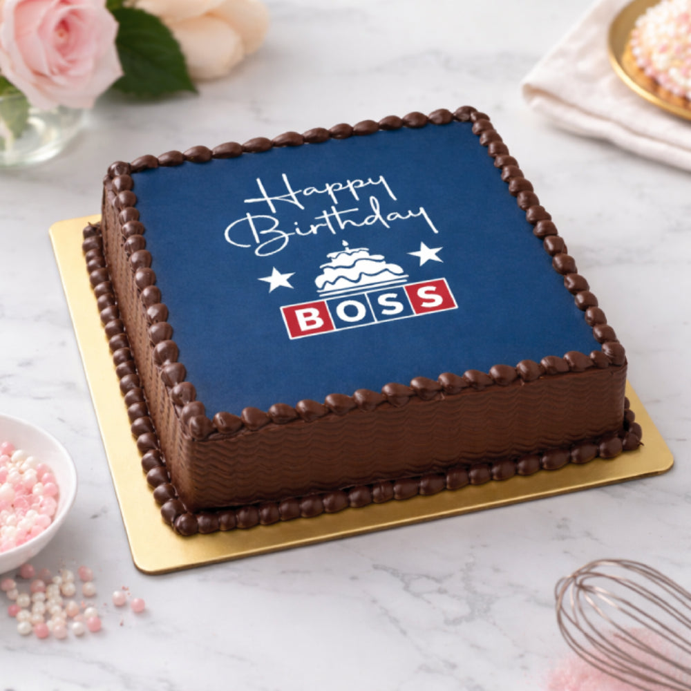 Square chocolate "Happy Birthday Boss" cake with navy blue edible print and decorative icing. top angle view