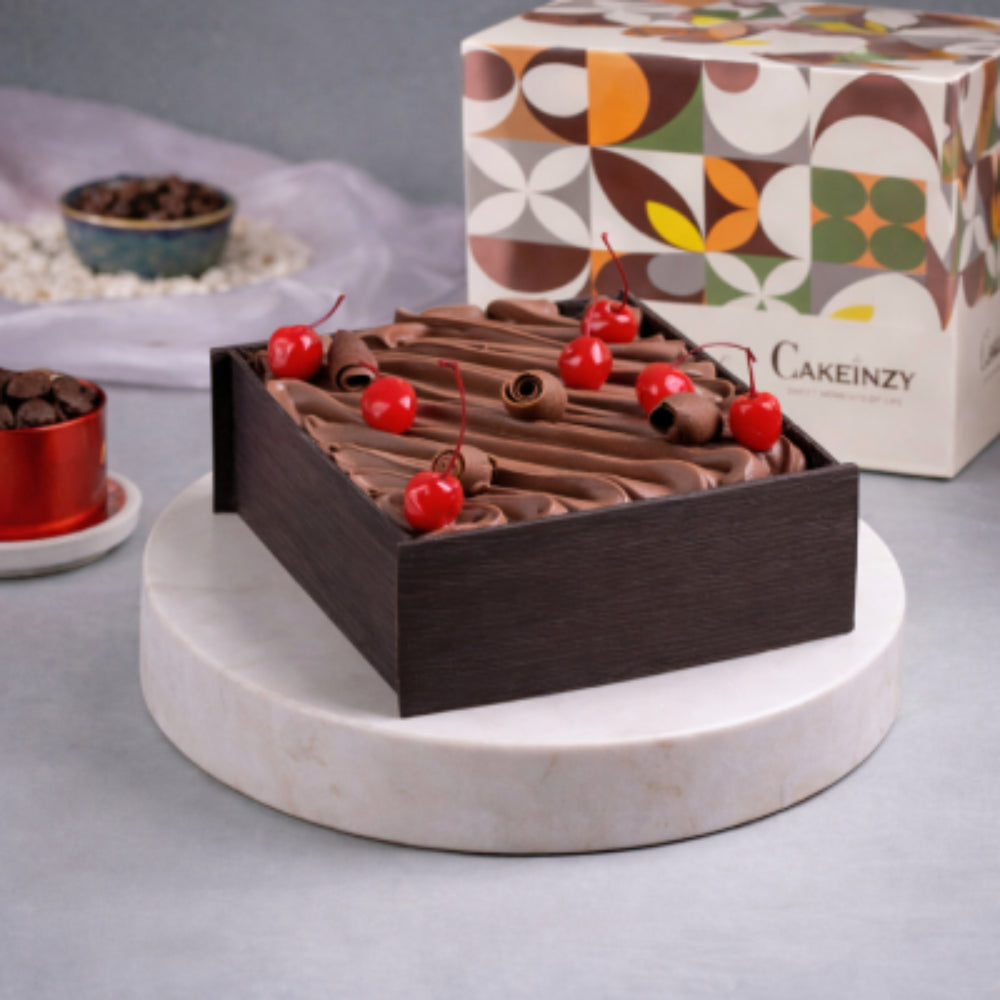 A square shape black forest cake with cherry toppings.