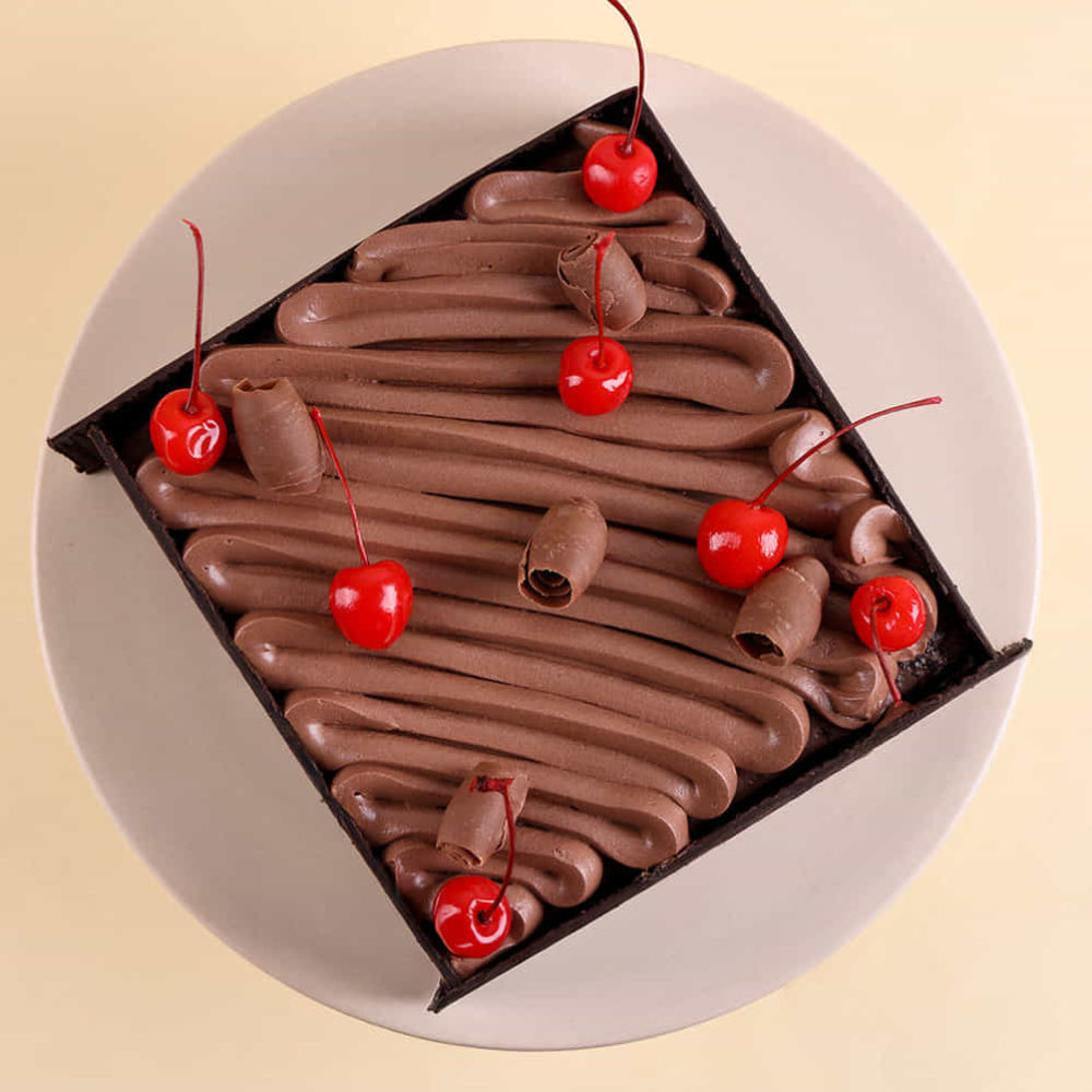 A square shape black forest cake with cherry toppings. top view