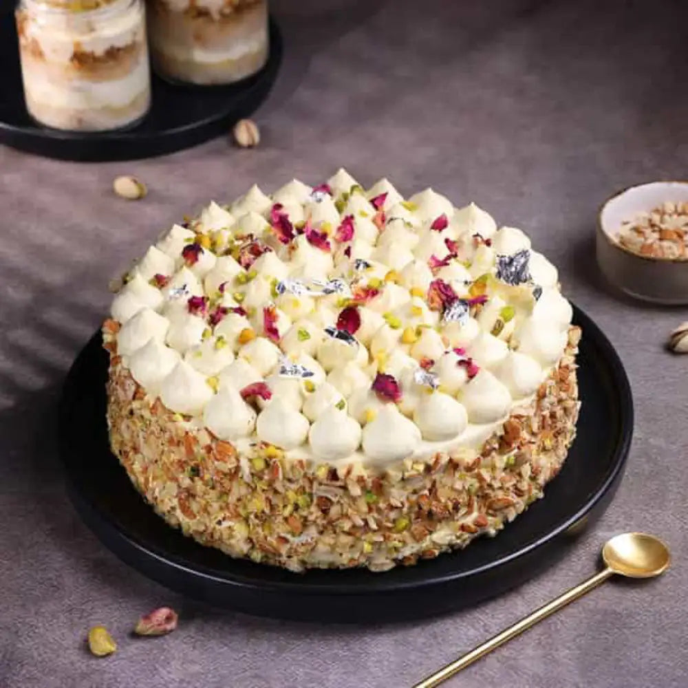 Elegant Thandai Gulkand Cake topped with rose petals, silver leaf, and crushed nuts.
