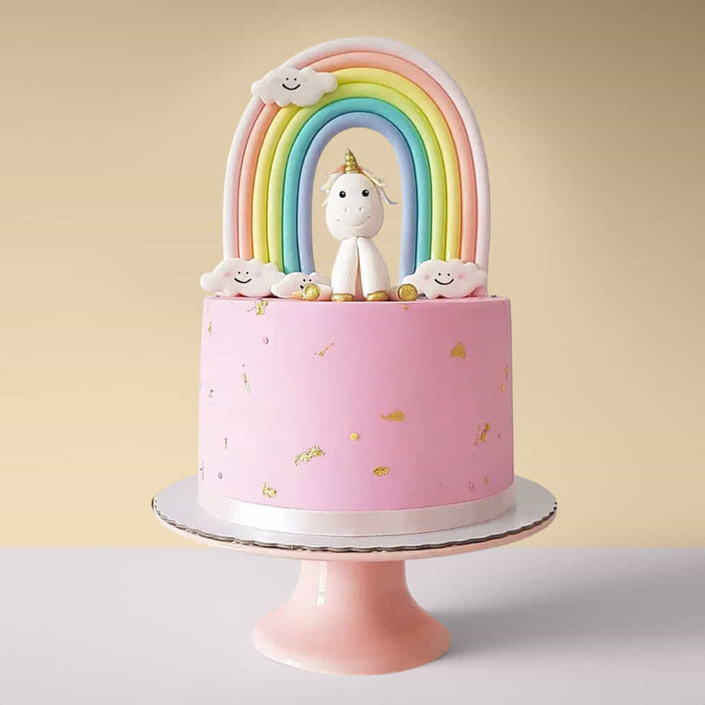 Pink cake with a unicorn and rainbow decoration on a stand against a yellow background