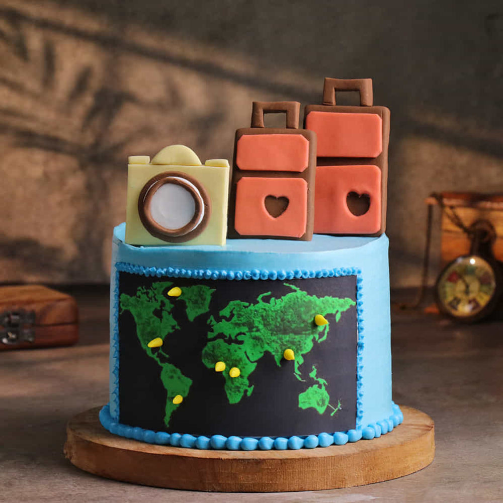 Blue travel cake with world map, camera, and suitcase toppers. side view