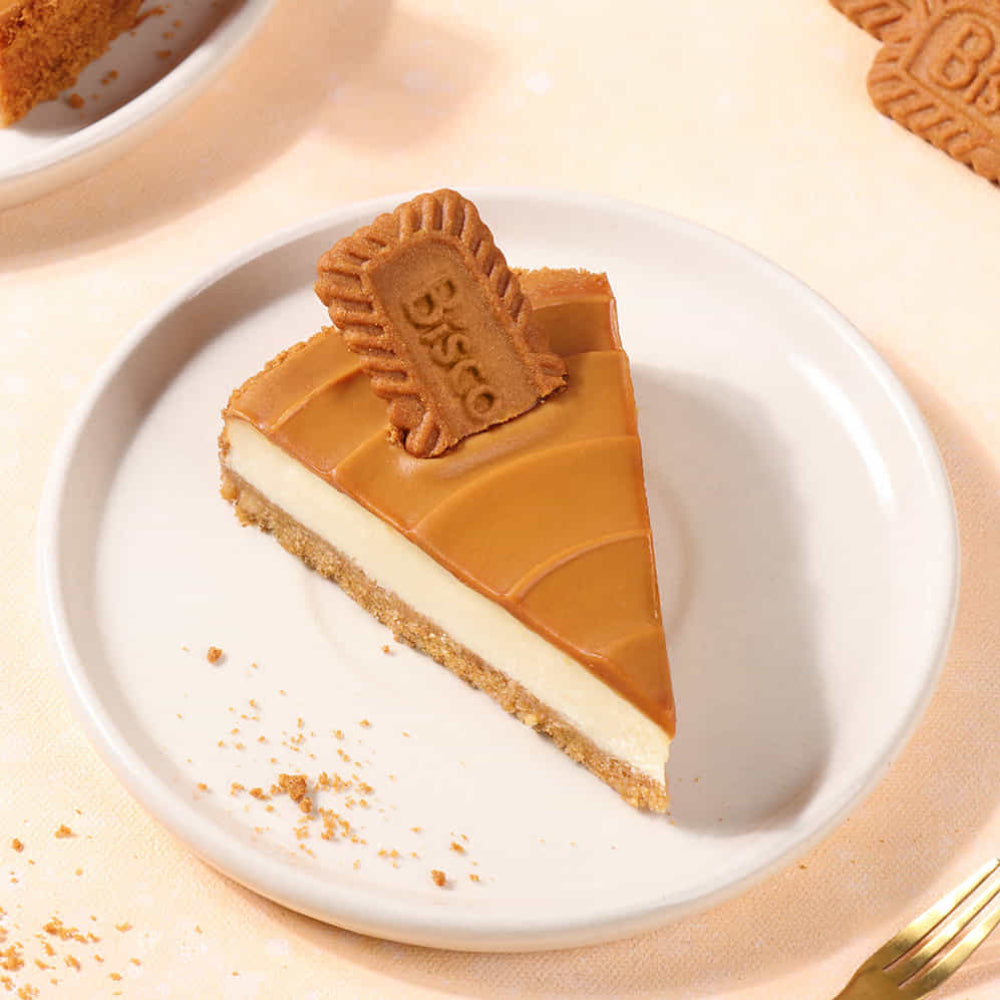 Slice of Biscoff cheesecake with creamy white filling, caramel topping, and a Biscoff cookie on a white plate.