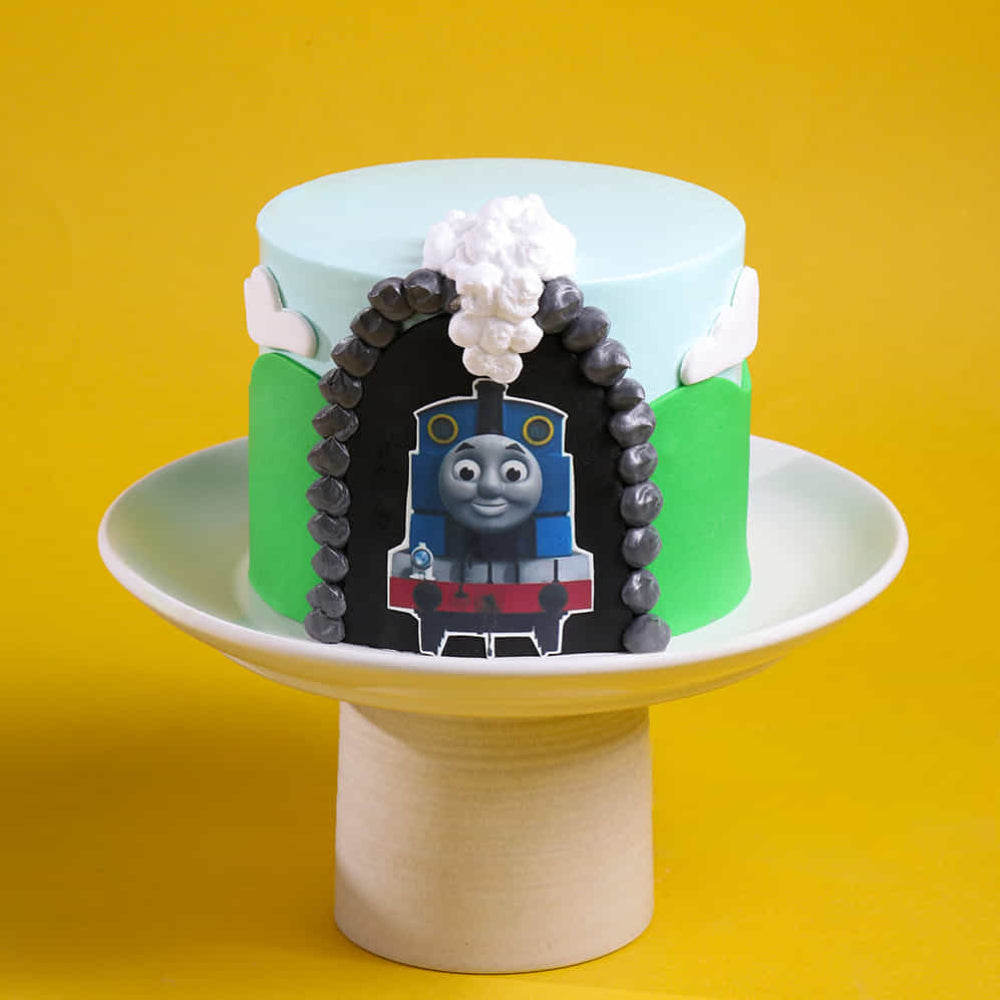 Custom Thomas & Friends birthday cake with edible train engine image, green hills, and cloud fondant decorations.